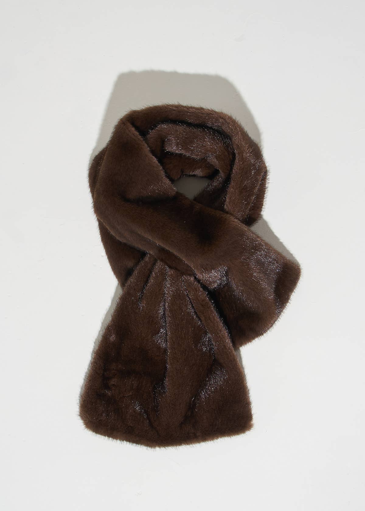 A dark brown faux fur scarf, styled in a loose knot, displayed on a light gray rectangular block against a white background.